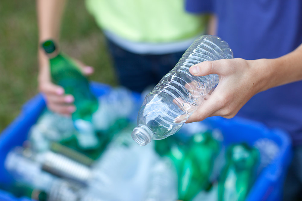 hands holding bottles over reycling bin Pederson Sanitation & Recycling Fort Dodge IA